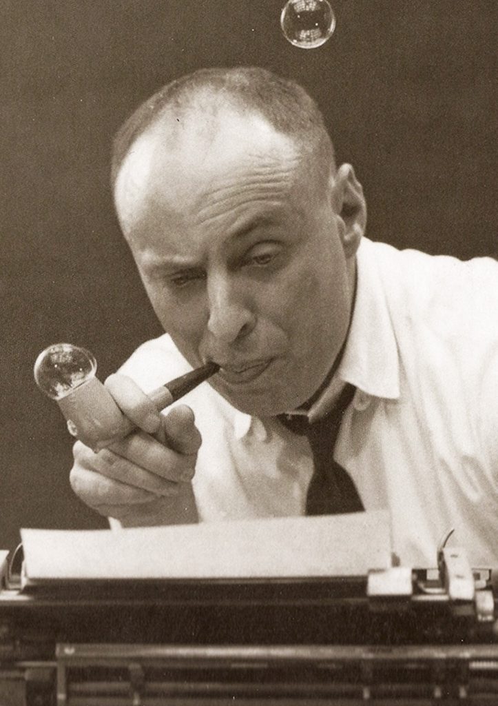 Portrait d’Harvey Kurtzman, pipe à la bouche, en train de souffler des bulles devant une machine à écrire. Figure fondatrice du magazine MAD et de la satire graphique américaine des années 1950.