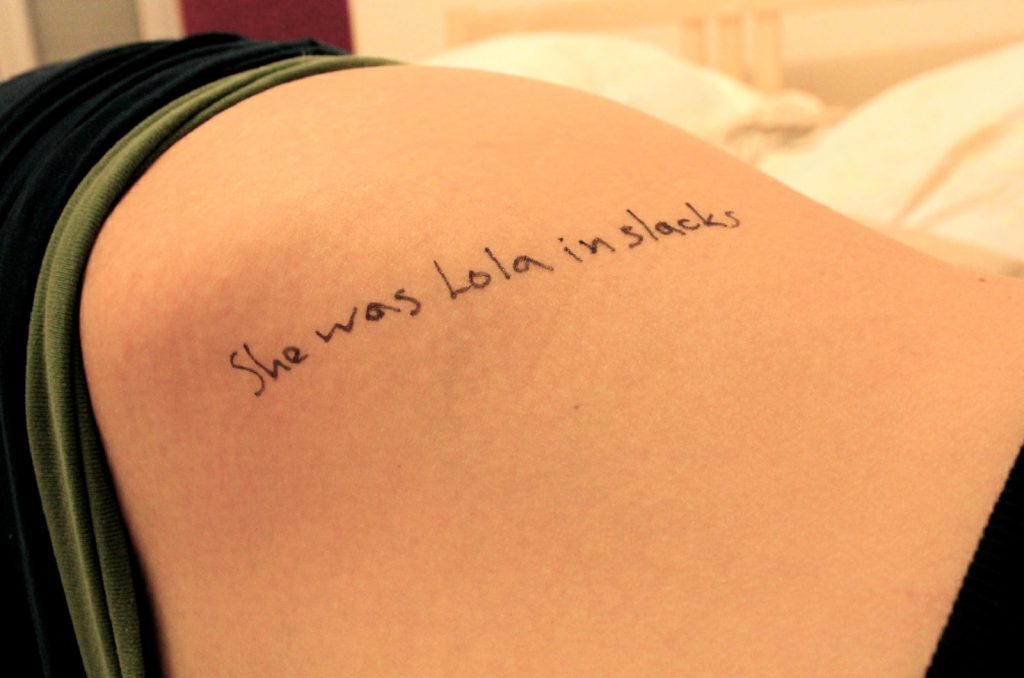 Gros plan sur le flanc d’une femme avec l’inscription manuscrite “She was Lo in slacks” écrite au marqueur noir.