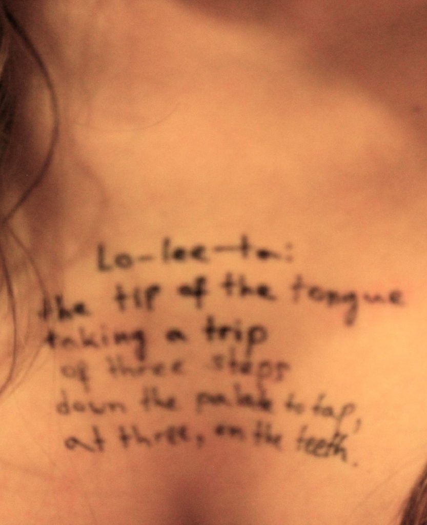 Gros plan sur la clavicule et le haut du torse d’une femme, avec une phrase manuscrite en anglais écrite au marqueur noir sur la peau.