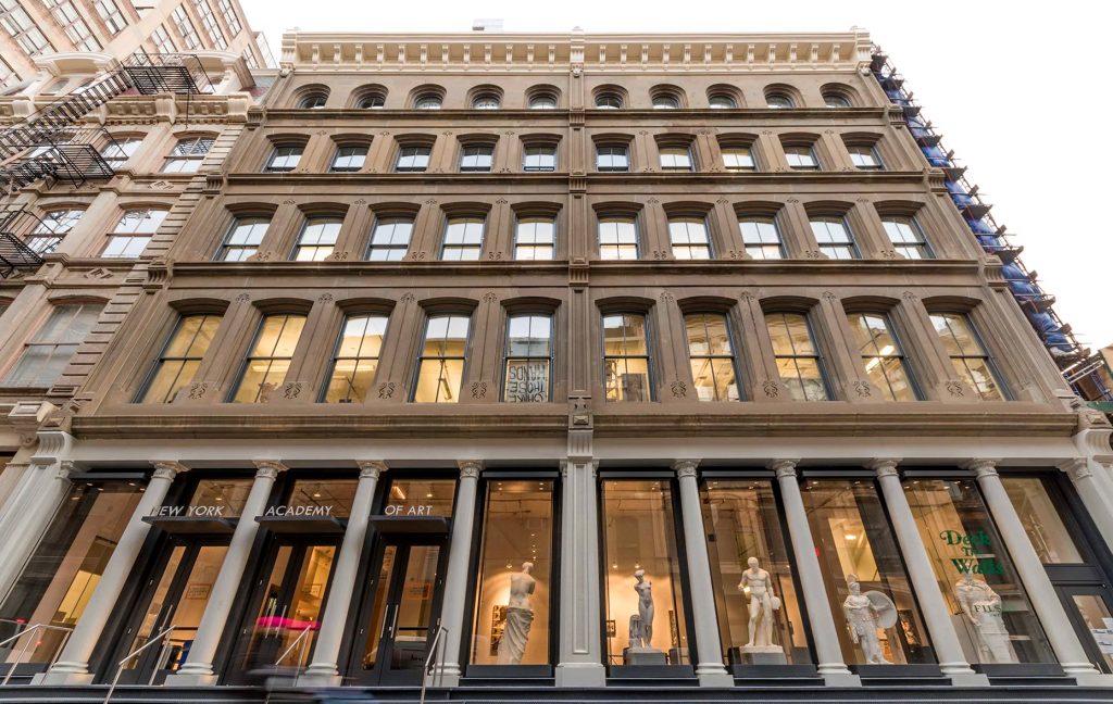Façade de la New York Academy of Art à New York, entrée vitrée et colonnes blanches, éclairage intérieur chaleureux.