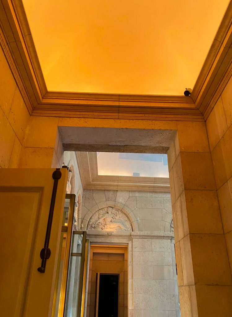 Chambre élégante avec lit double, murs décorés de motifs floraux bleus et rideaux rayés ; une caméra est placée discrètement près du plafond.