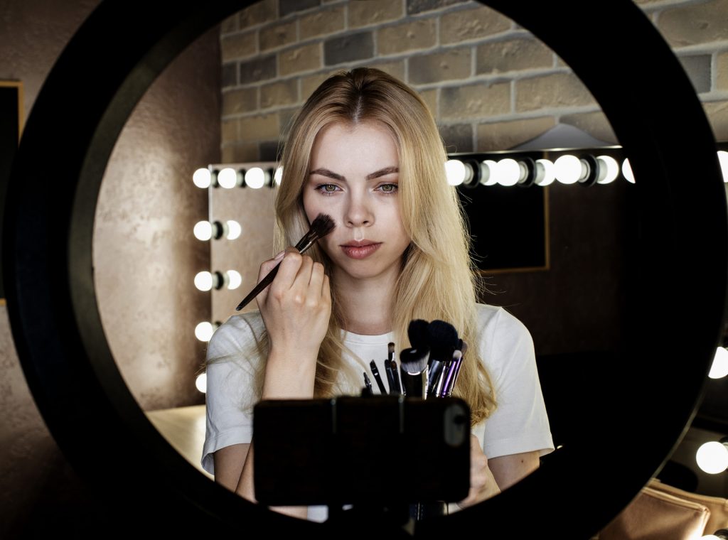 Femme se maquillant devant un smartphone avec un ring light dans une scène de création de contenu