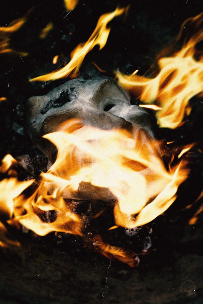 Photographie des faux-semblants : masque blanc de théâtre dans les flammes.